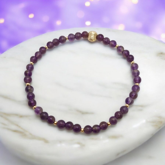 Purple beaded bracelet with gold accents on a marble surface with a purple gradient background