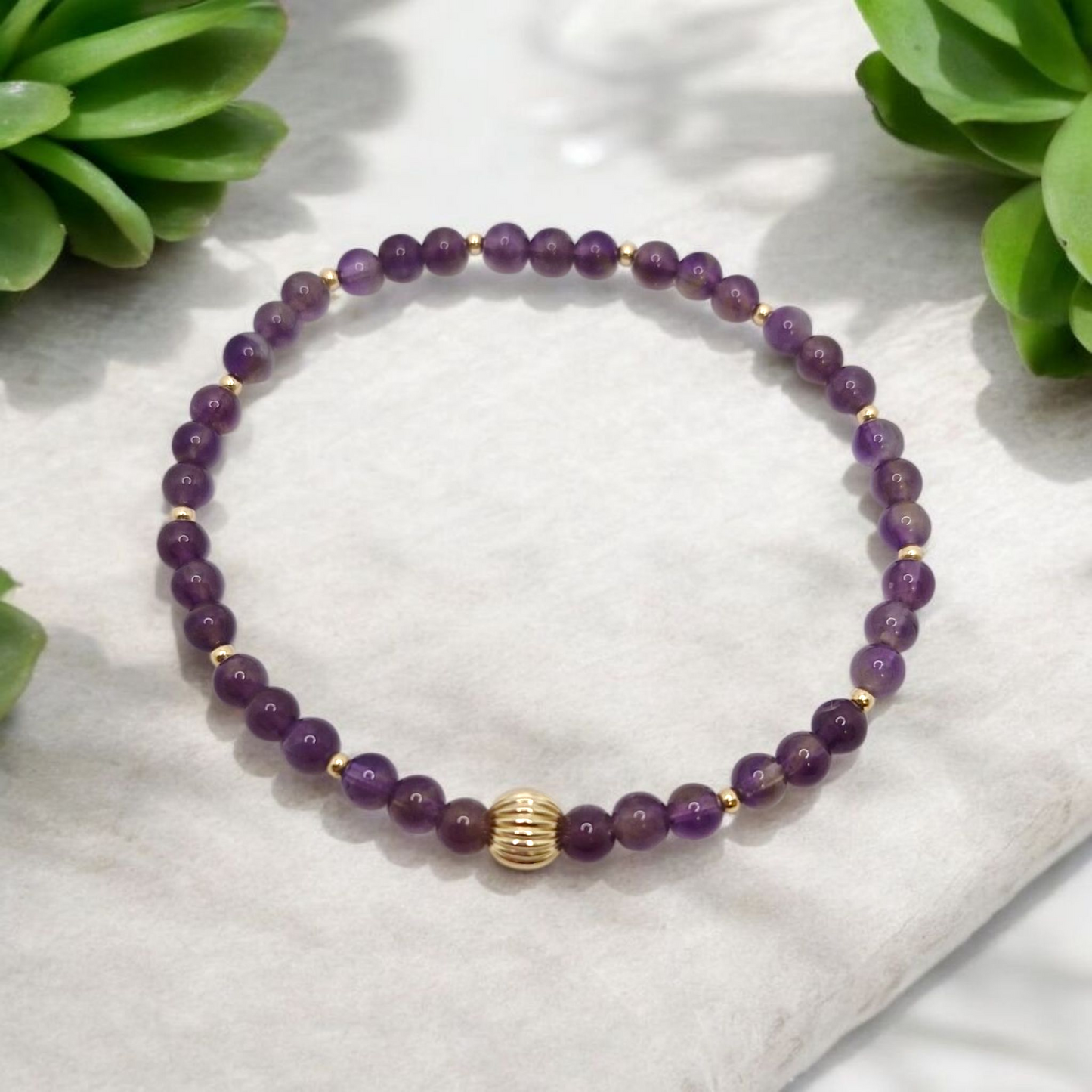 Purple beaded bracelet with a gold accent on a white stone surface with green plants in the background