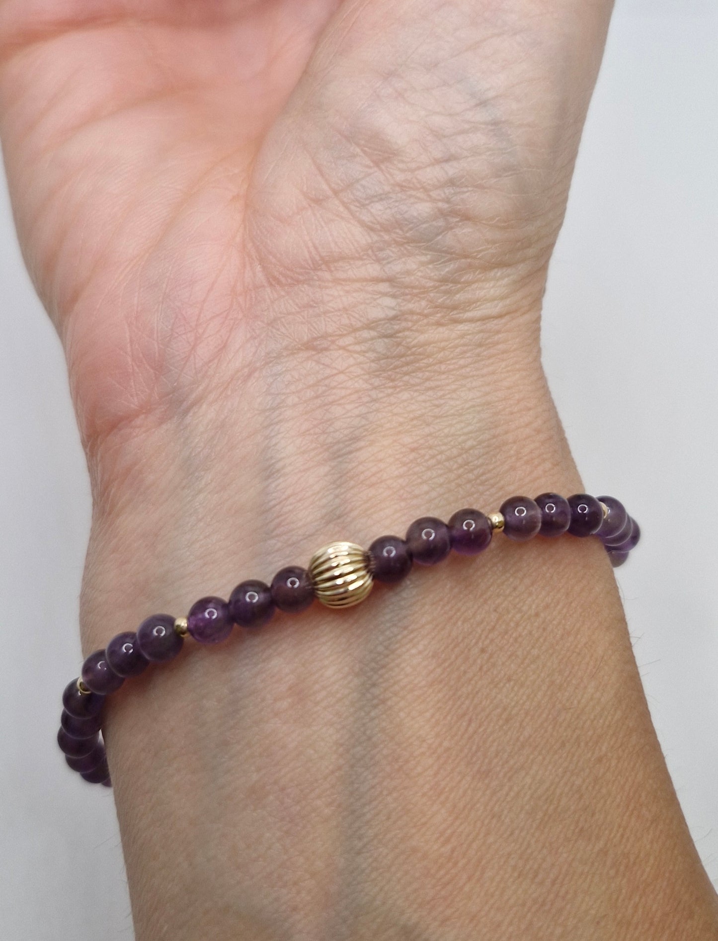 Purple beaded bracelet with a gold clasp on a wrist against a white background
