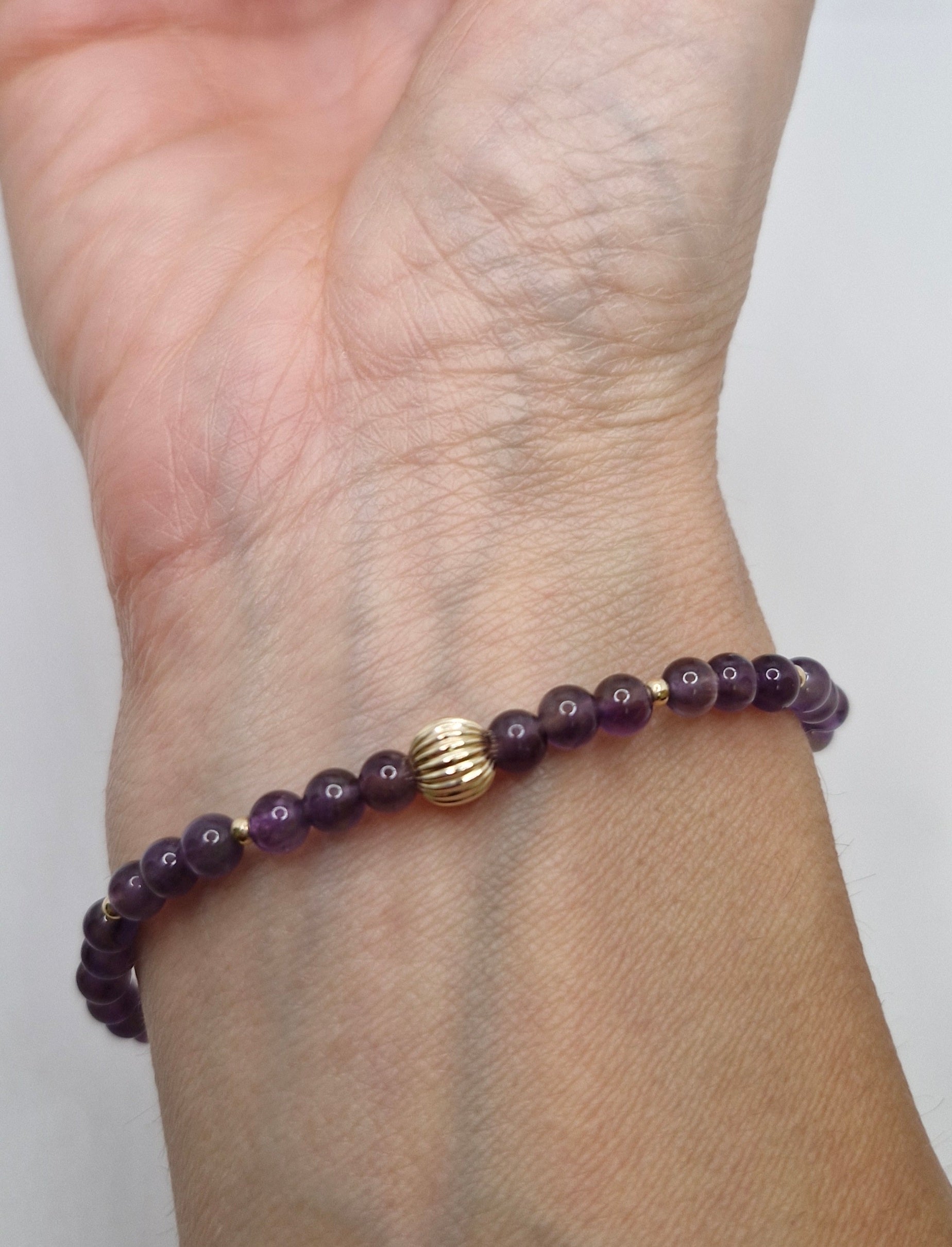 Purple beaded bracelet with a gold clasp on a wrist against a white background