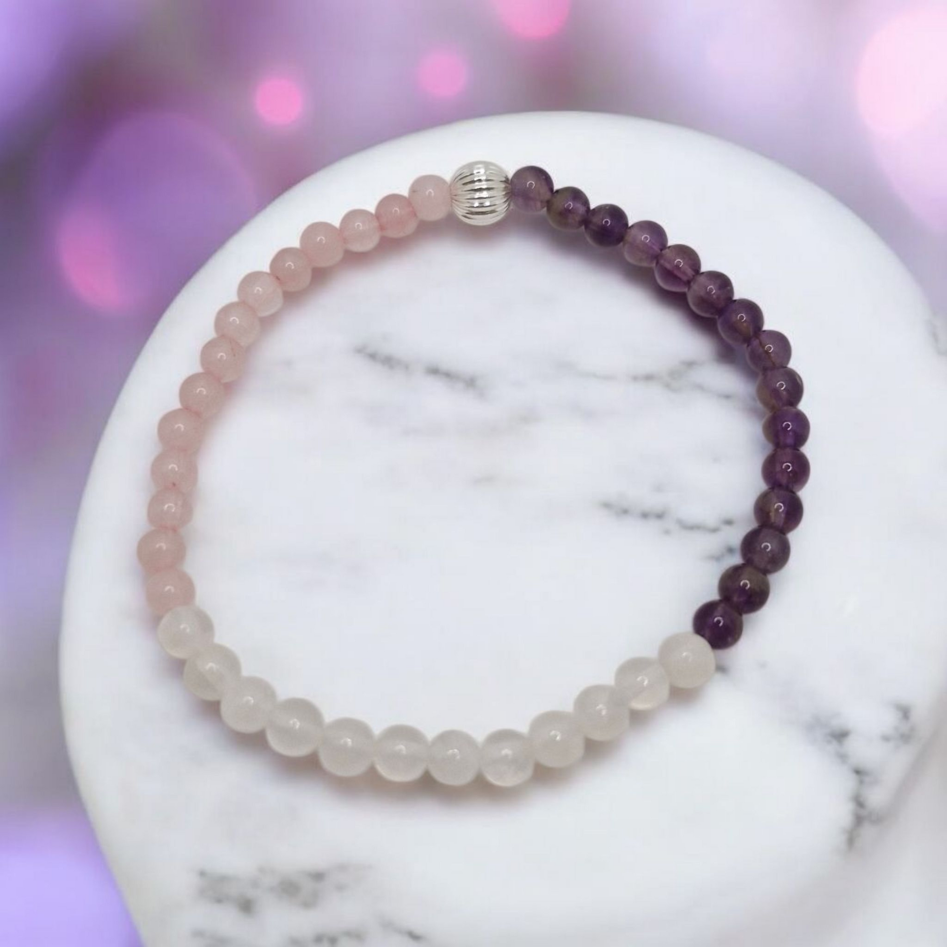 Beaded bracelet with purple and white beads on a marble surface with a blurred pink background