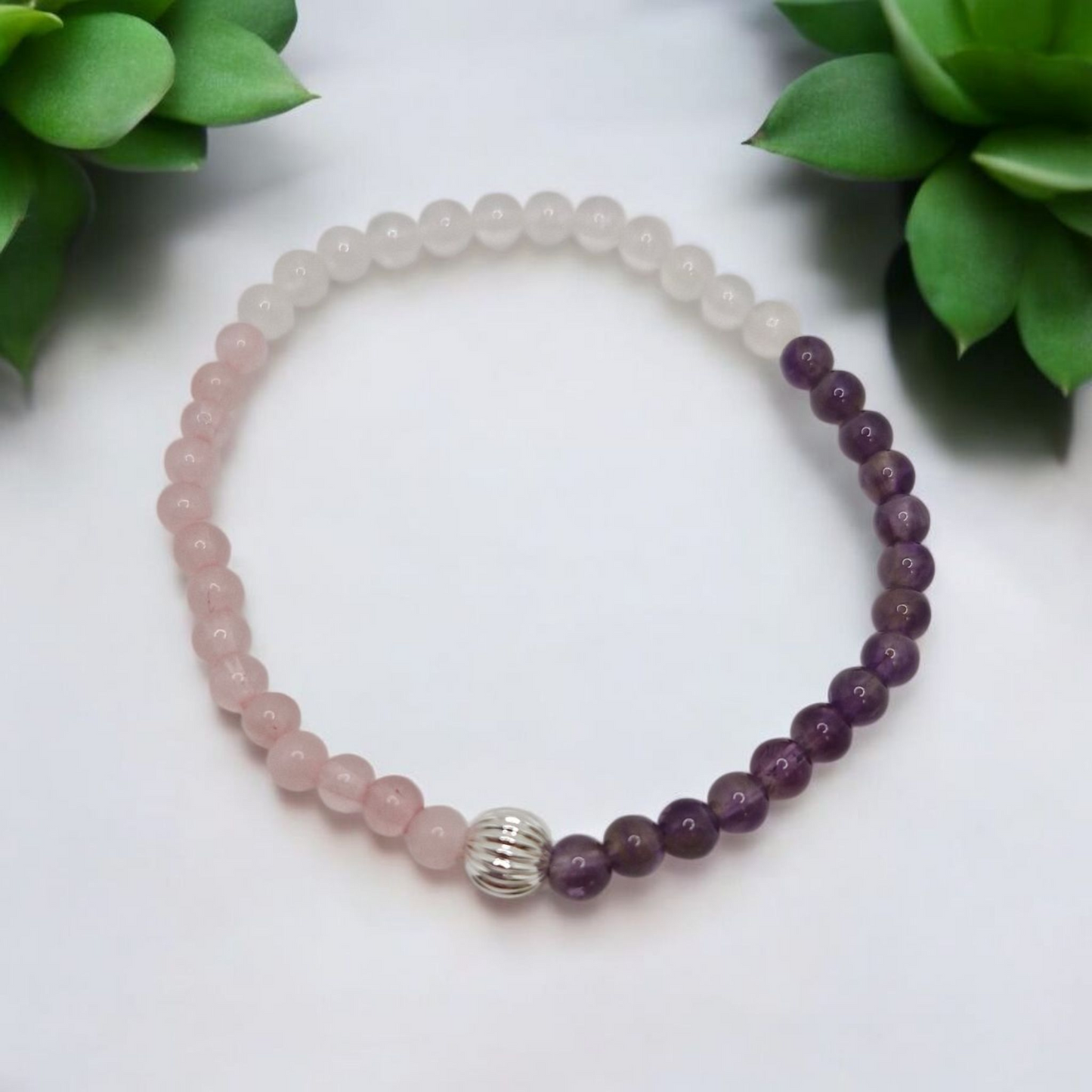 Beaded bracelet with pink and purple beads on a white background with green leaves.