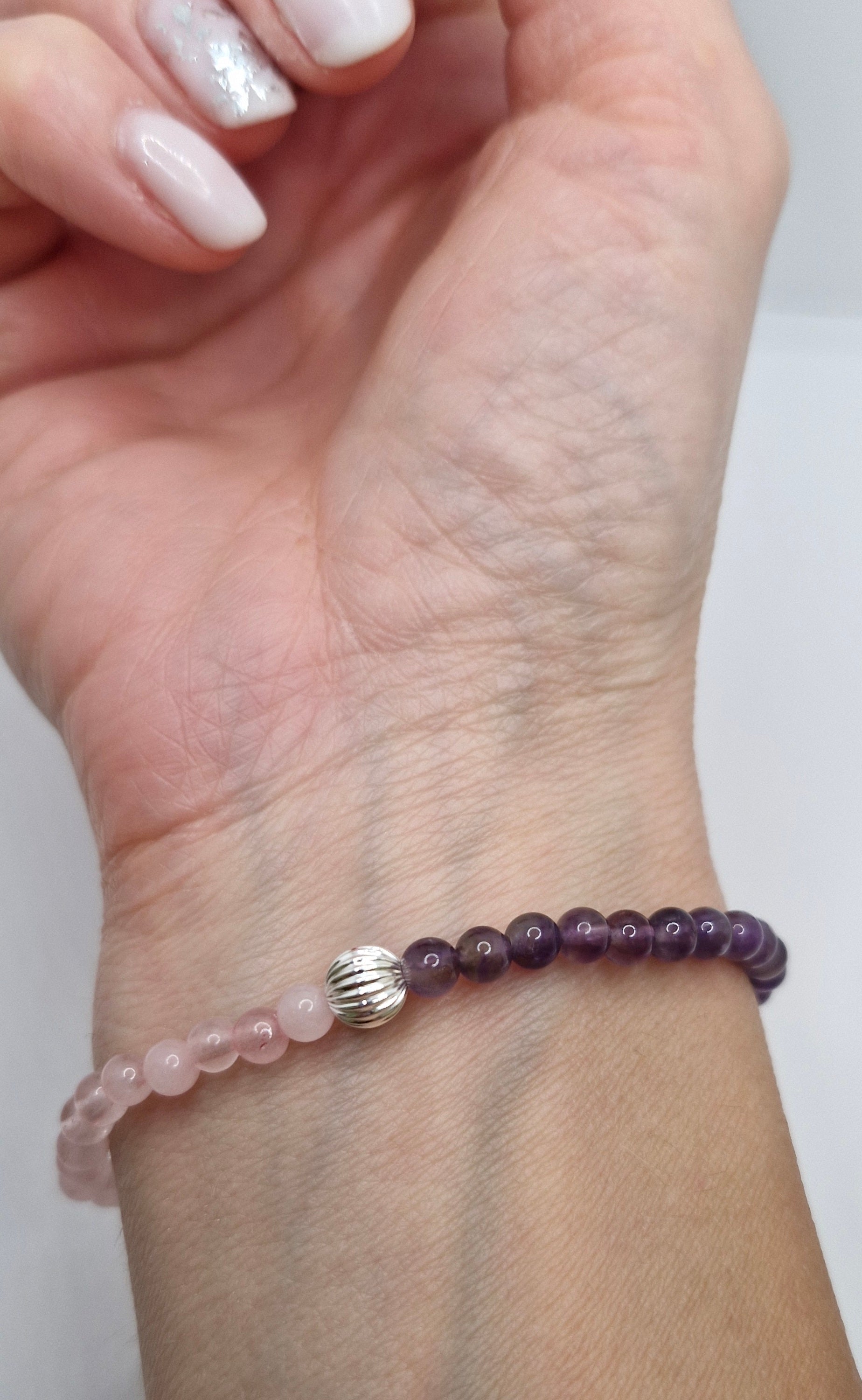 Hand wearing a beaded bracelet with a silver charm on a plain background