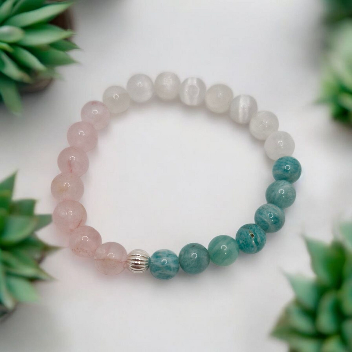 Beaded bracelet with pink and green stones on a white surface with plants in the background