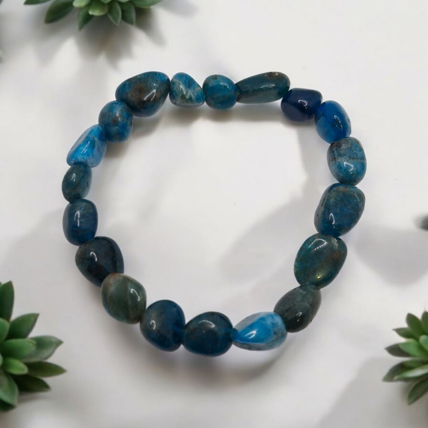 Blue beaded bracelet on a white background with green leaves