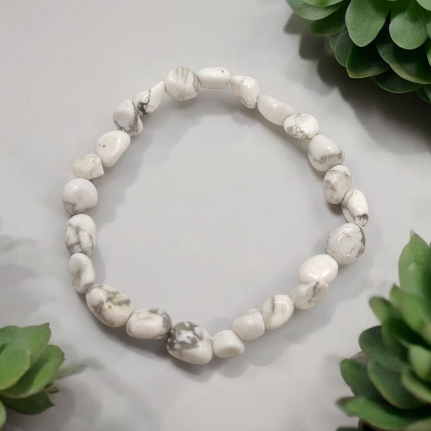 White beaded bracelet on a light gray surface with green leaves in the background