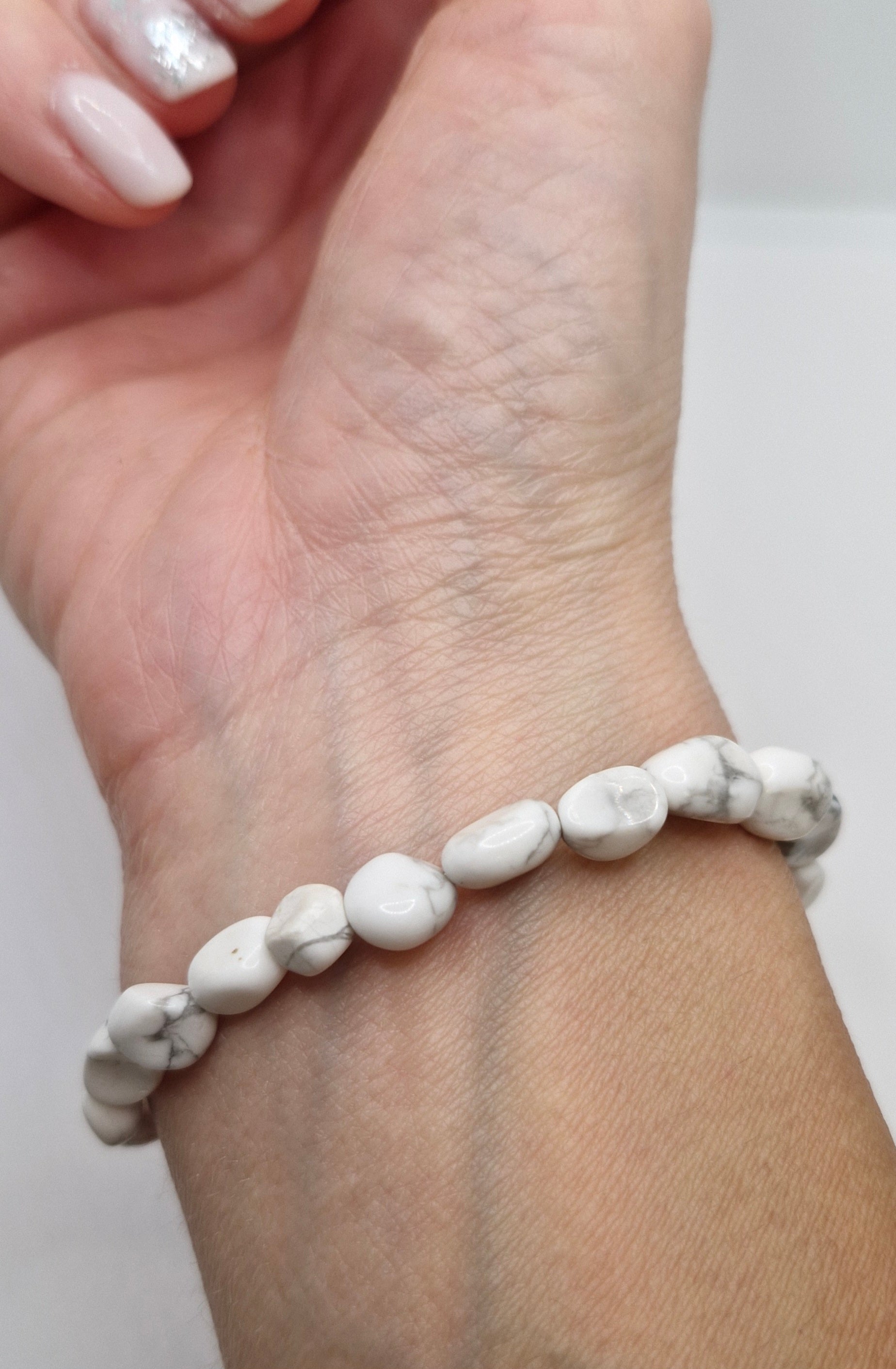 White beaded bracelet on a wrist with a plain background