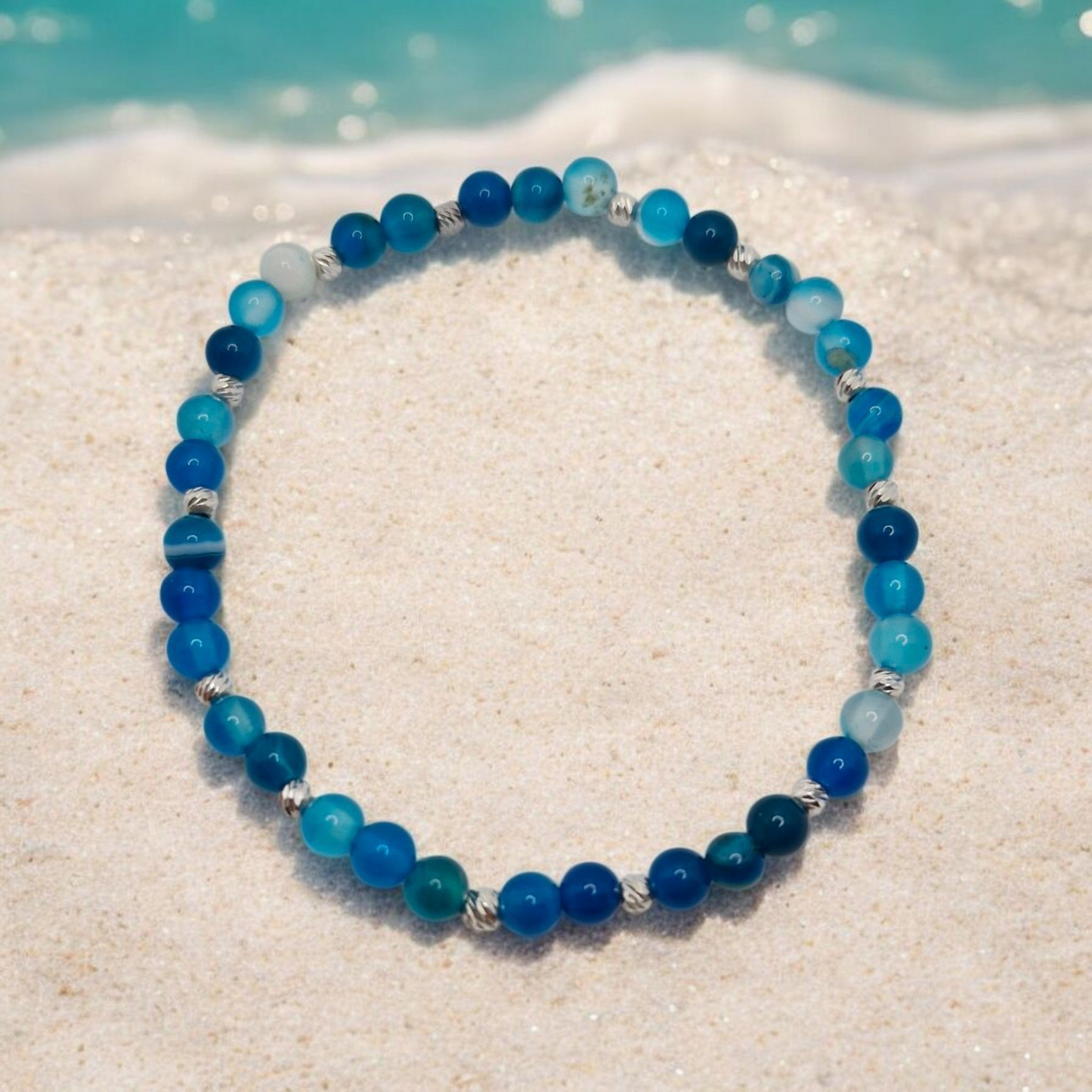 Blue beaded bracelet on a sandy surface with a beach background