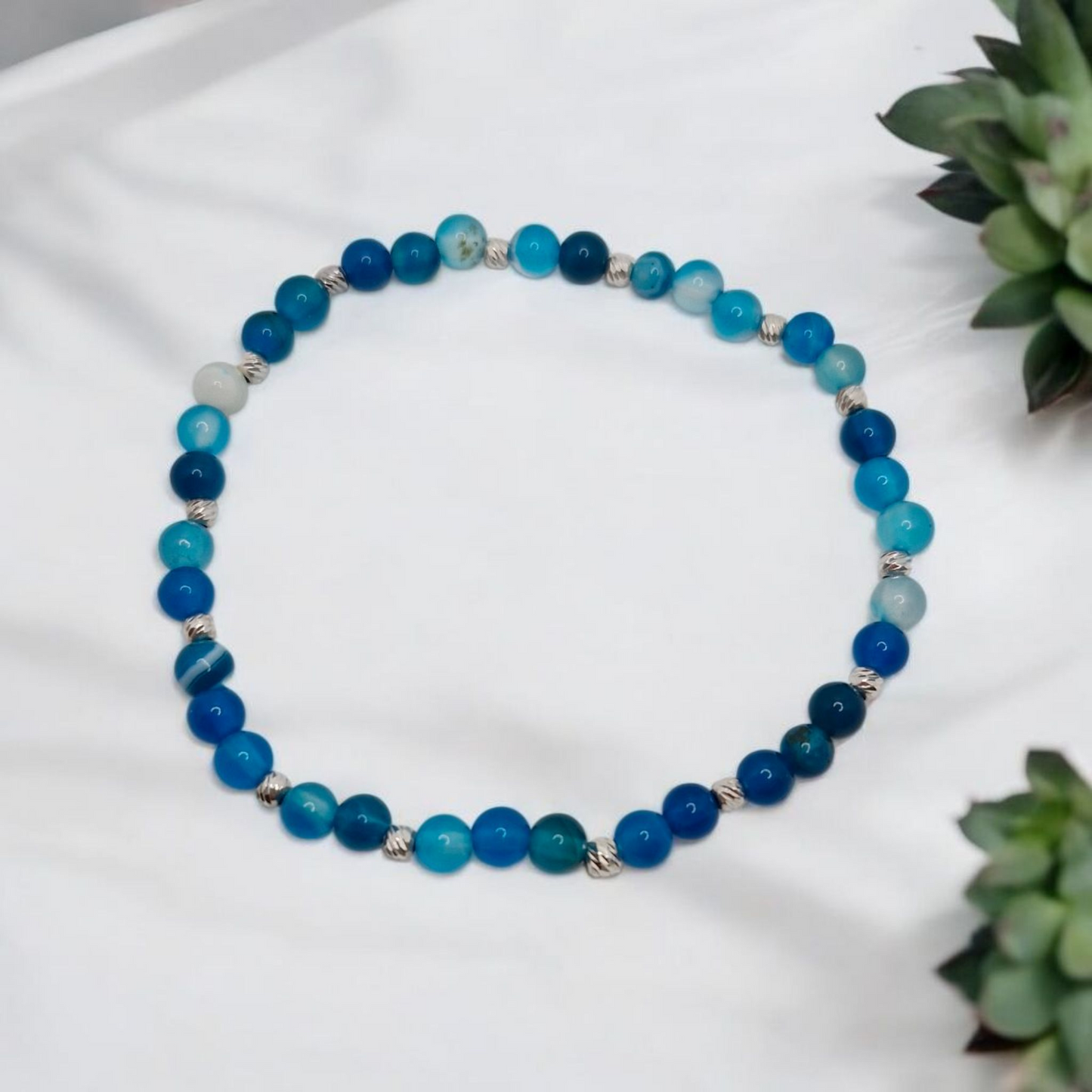 Blue beaded bracelet on a white surface with green plants