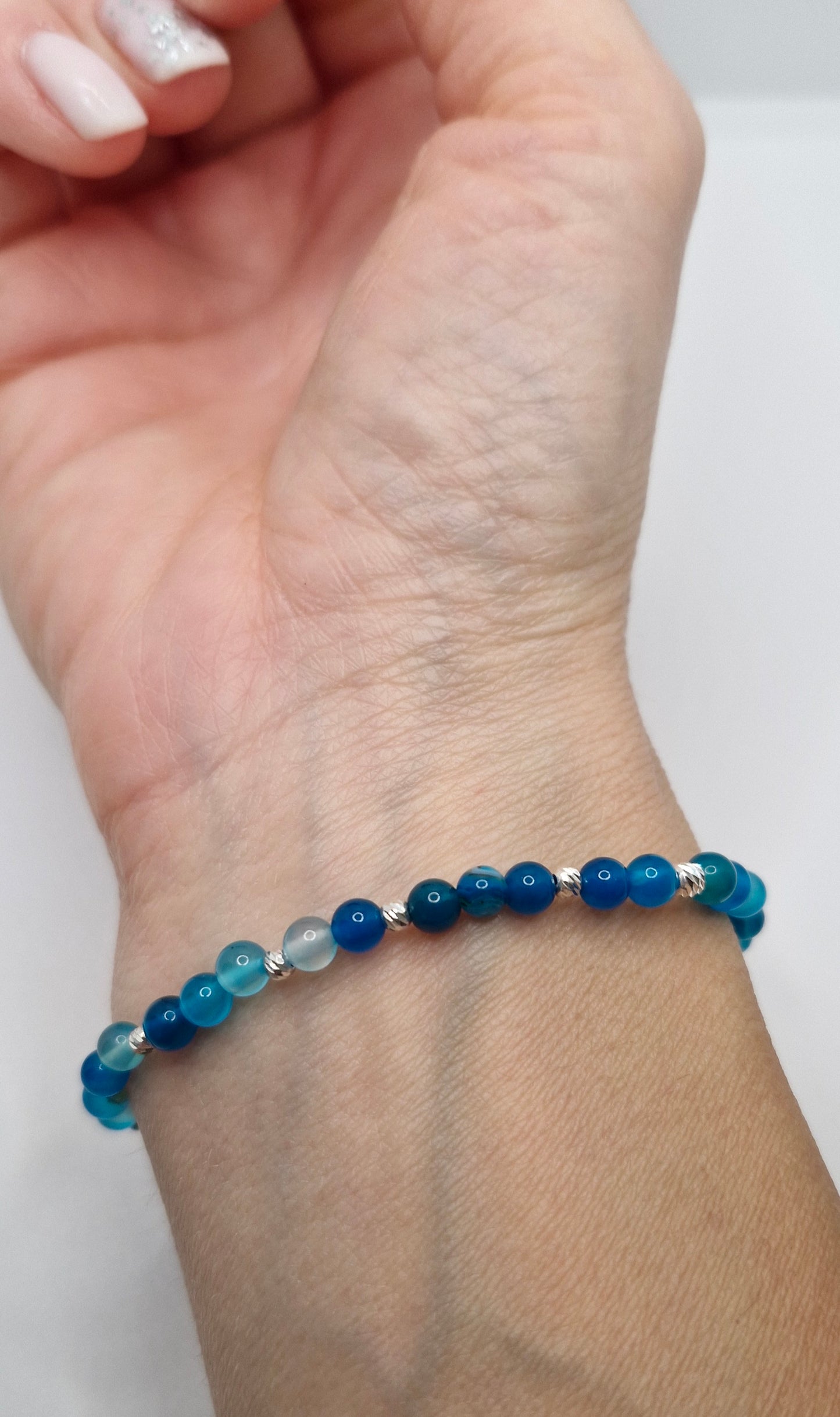 Hand wearing a blue beaded bracelet on a white background