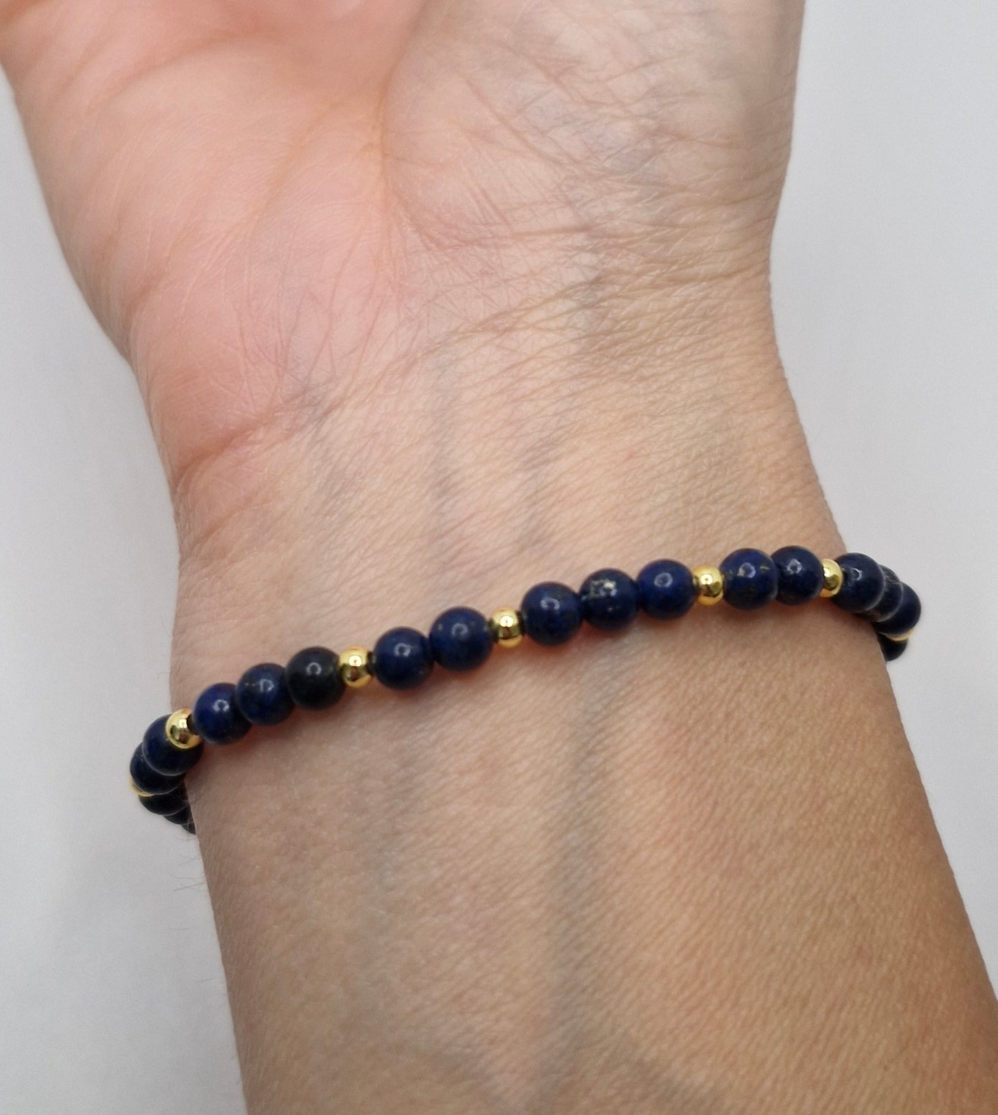 Navy blue beaded bracelet with gold accents on a wrist against a white background