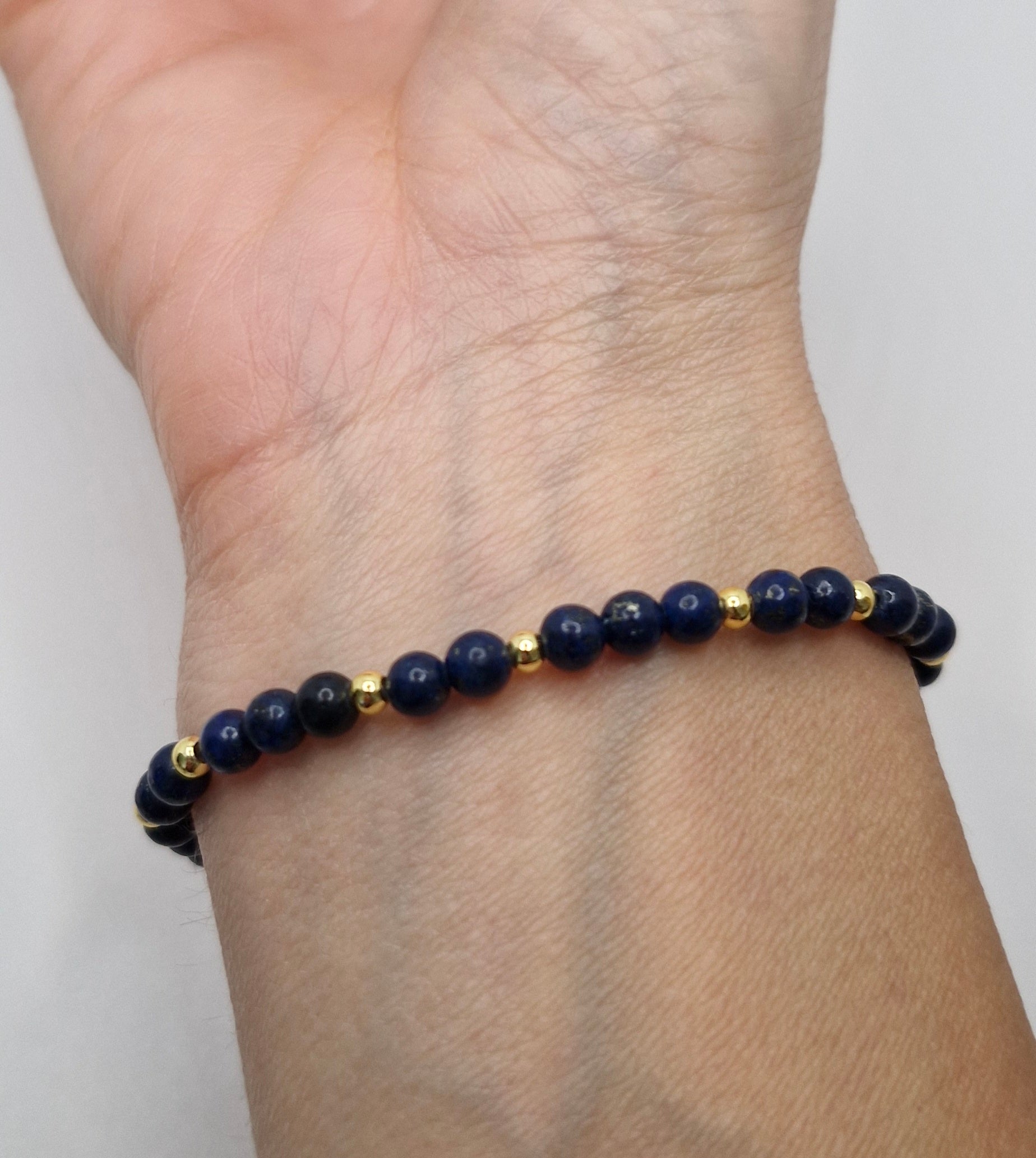 Navy blue beaded bracelet with gold accents on a wrist against a white background