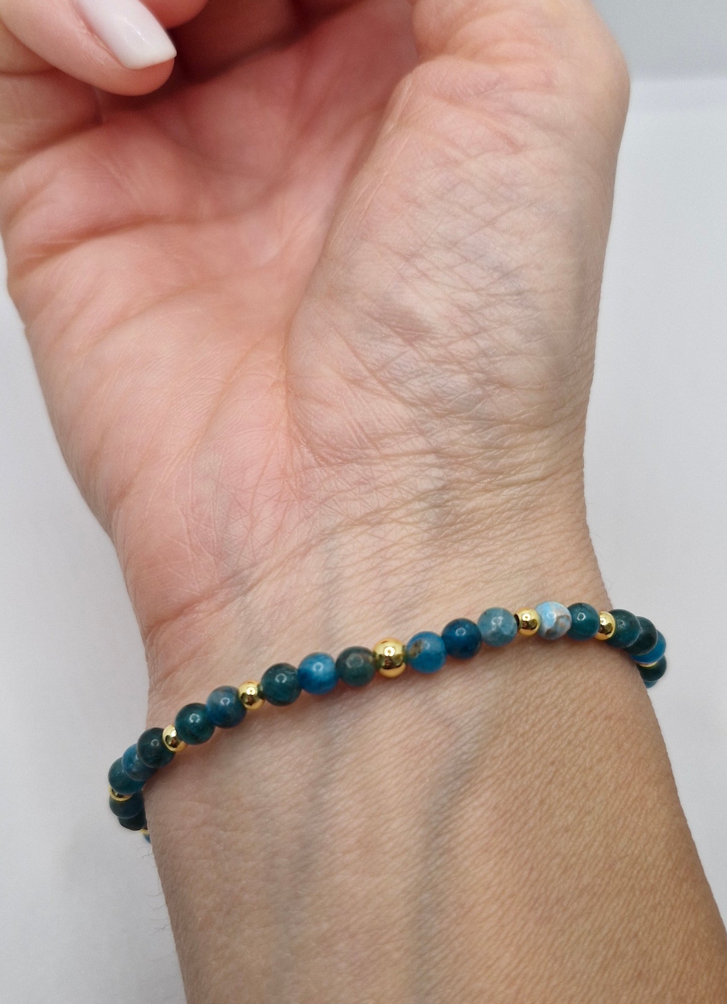 Hand wearing a blue beaded bracelet with gold accents on a white background