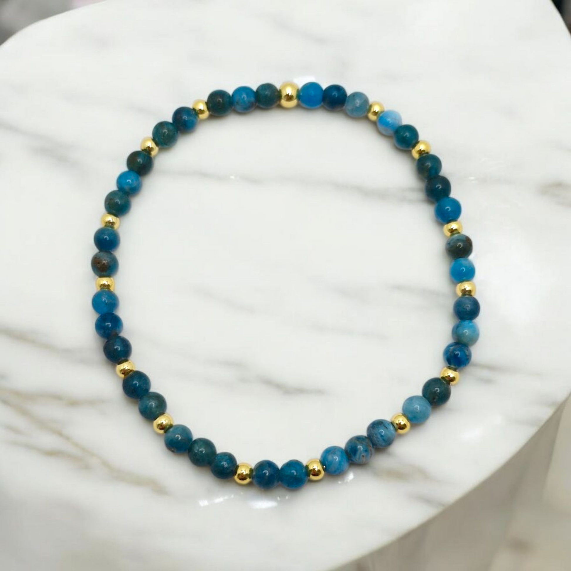 Blue beaded bracelet with gold accents on a white marble surface