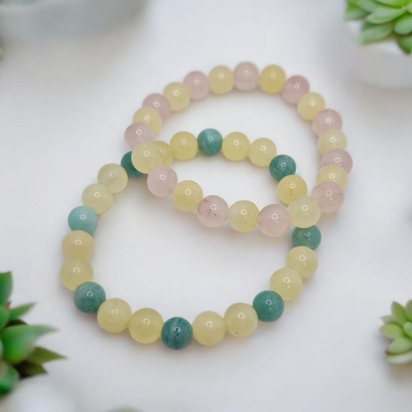 Set of pastel-colored beaded bracelets on a white surface with green plants in the background