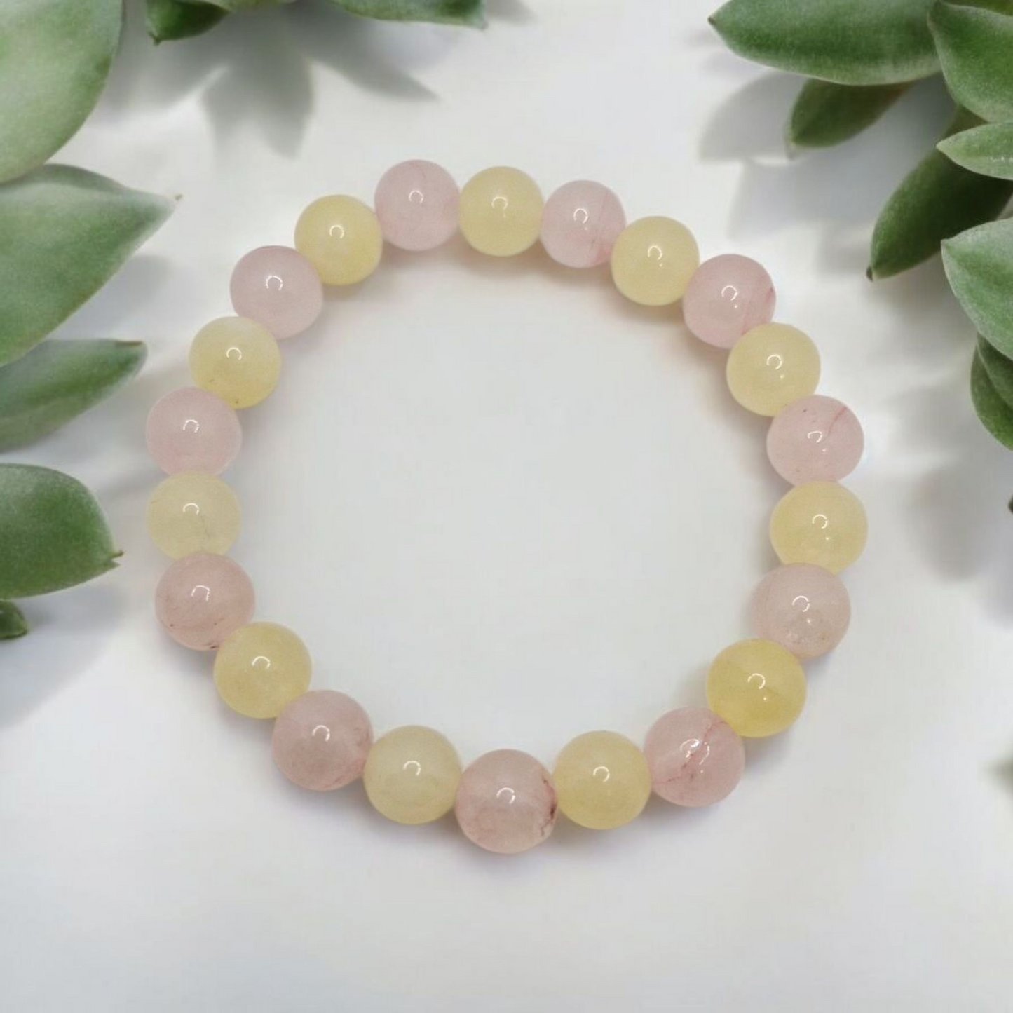 Beaded bracelet with pink and yellow beads on a white surface with green leaves in the background