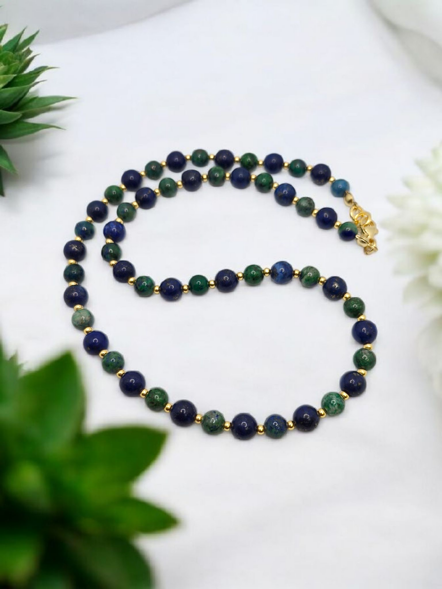 Necklace with blue and green beads on a white surface with plants in the background