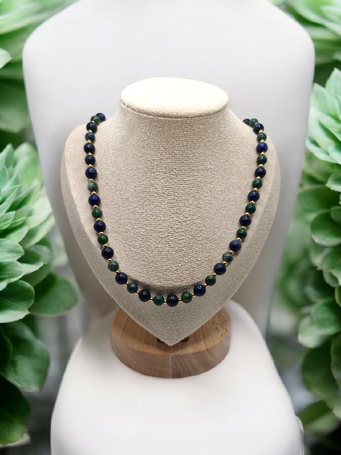 Necklace with green and black beads on a wooden and beige mannequin bust against a green foliage background