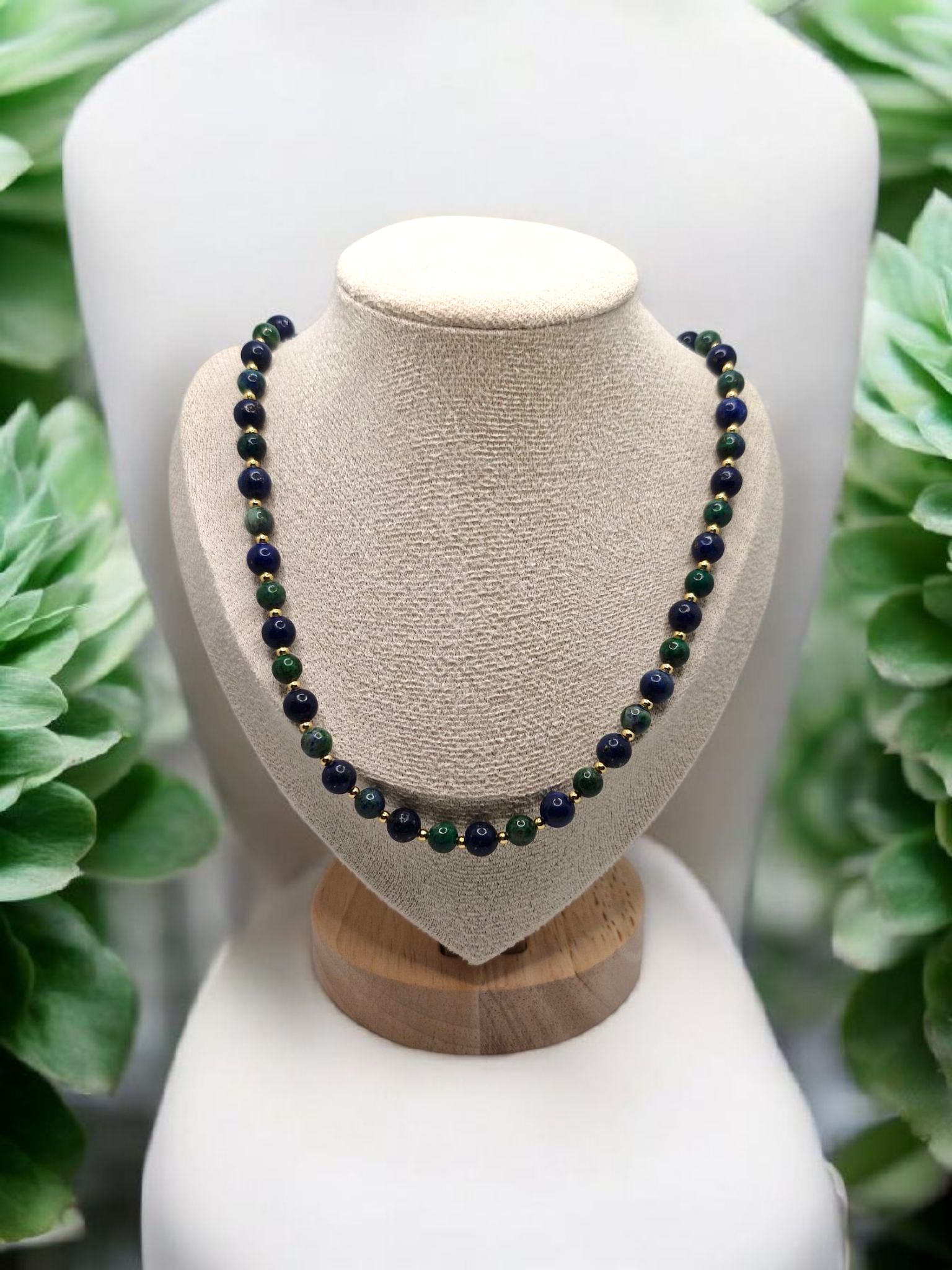 Necklace with green and black beads on a wooden and beige mannequin bust against a green foliage background