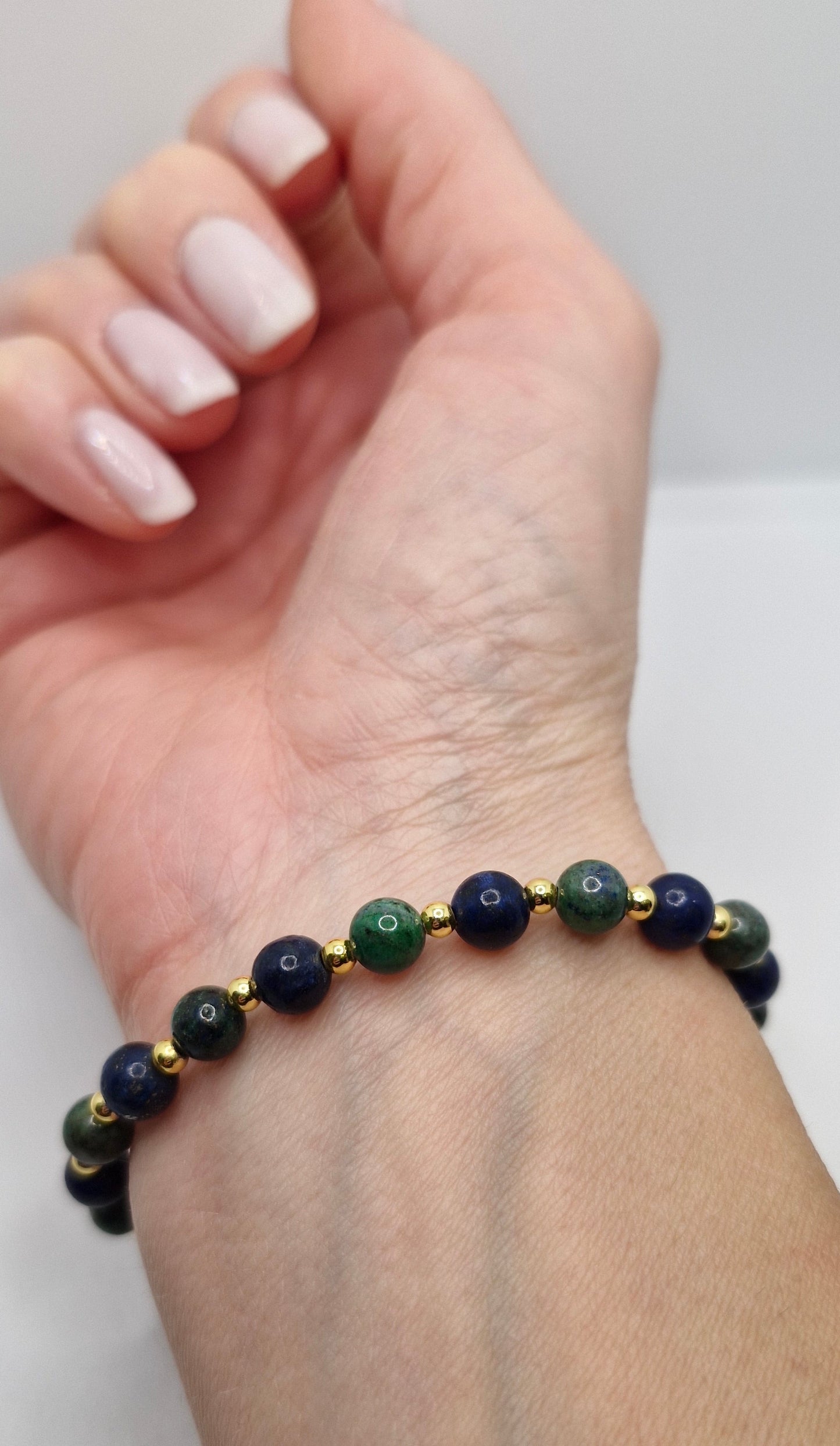 Hand wearing a bracelet with blue and green beads on a plain background