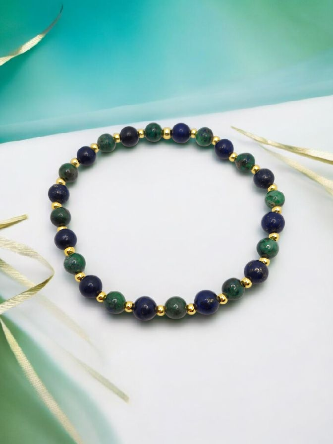 Beaded bracelet with green and blue beads on a white surface with gold accents