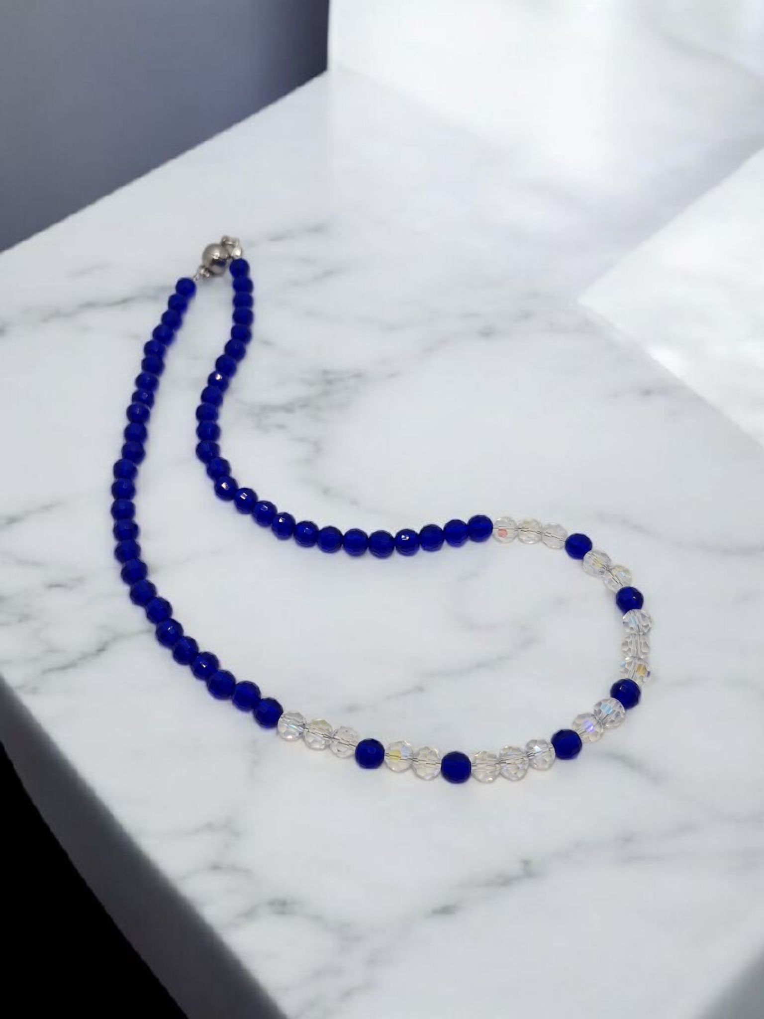 Necklace with blue beads and silver clasp on a marble surface